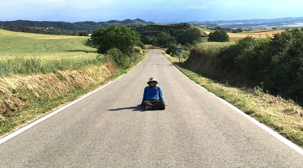 Juan durante el Camino de Santiago, sentado en una carretera entre campos